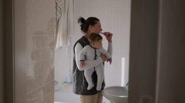 Anne, bebeği kollarında tutarken dişlerini fırçalarken, birden fazla işi üstlenirken ve kendine bakarken, aile banyosunda bağ kurarken, sakin ve odaklanmış bir anda,