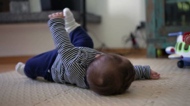 Bebek yerde yatıyor, kollar havada yuvarlanmaya çalışırken motor beceriler, güç ve koordinasyonla ilgili erken gelişim kilometre taşını gösteriyor.
