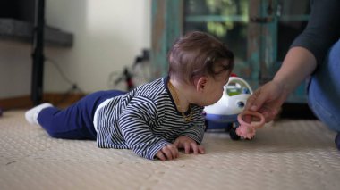 Bebek yerde yatıyor, başını ve vücudunun üst kısmını kaldırırken bakıcılara doğru dönüyor, güç, merak ve bağlılık ile ilgili erken gelişim kilometre taşlarını gösteriyor.