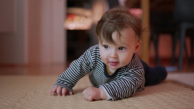 Bebek mindere uzanıyor, kollara dayanıyor, garip ifade, çevreyi keşfetme, gelişim göbeği aktivitesi, ev içi ortam, erken motor becerilere odaklanıyor.