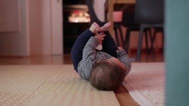 Bebek yerde yatıyor, kollarını açmış yuvarlanıyor, oyun zamanı boyunca aktif hareket ediyor, fiziksel koordinasyonu keşfediyor, ev ortamında erken gelişim kilometre taşı.