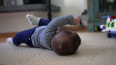 Bebek yerde yatıyor, kollar havada yuvarlanmaya çalışırken motor beceriler, güç ve koordinasyonla ilgili erken gelişim kilometre taşını gösteriyor.