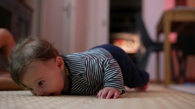 Bebek yerde yatıyor, kollarıyla yukarı itiyor, heyecanlı bir ifadeyle ağzı açık, neşeli bir an yaşıyor, erken motor becerilerini gösteriyor, kapalı alanda enerjik bir ortam.