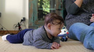 Bebek merakla yerde yatıyor, ön kollara dayanıyor, çevreyi gözlemliyor, oyuncak uçak yakınlarda, erken gelişim ve keşif gösteriyor.