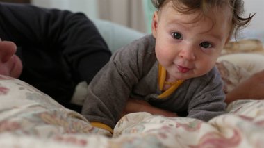 Bebek yatakta yatarken garip bir ifadeyle uzanıyor, annesinin koluyla destekleniyor, çevreyi keşfediyor, hassas aile bağları, sıcak ev ortamları, erken gelişim