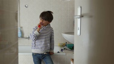 Banyoda dişlerini fırçalayan genç bir çocuk, günlük hijyen rutini, bağımsız kişisel bakım, diş sağlığı, çocukluk alışkanlıkları, samimi günlük bakım, kapalı alanda kişisel bakım