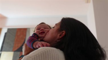 Anne havadayken bebeği öpüyor. Sevgi ve kahkaha dolu neşeli bir an. Ev ortamında samimi bir aile ortamı.
