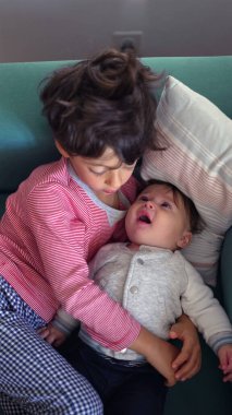 Kanepede bebeğe sarılan genç çocuk, şefkatli kardeş kucaklaşması, sevinçle gülümseyen bebek, içten aile bağı, sevecen bağ, sıcak ve rahat ev ortamında sevgi.