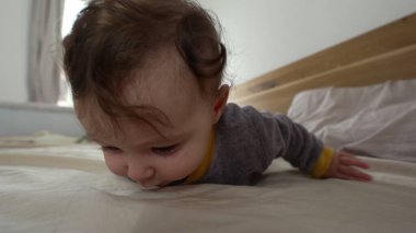 Bebek yatakta yüzüstü yatıyor, kollarını kaldırıyor ve tuhaf bir ifadeyle yan yana bakıyor, erken motor beceri geliştirme, kapalı bir aile ortamı, keşif ve büyüme.