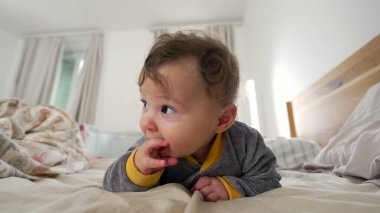 Bebek yatakta karnının üstüne yatar, kısık sesle gülümserken ağızdan ağıza neşeli ve meraklı bir ifade, sıcak bir aile anı, erken çocukluk gelişimi ve keşifler.