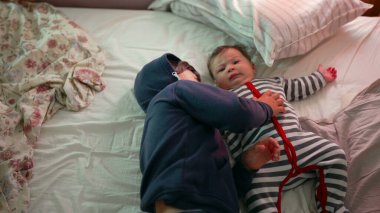 Ağabeyim bebek kardeşiyle yatakta yatıyor, hassas bir anı paylaşıyor, sıcak bir ev ortamında birbirine bağlanıyor ve dinleniyor.