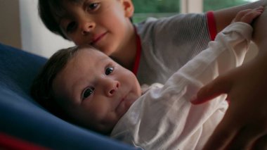 Büyük kardeş bebeği sıkıca tutuyor, güçlü kardeş kucaklıyor, koruyucu ama ezici, çocukluk yakınlığı, aile bağı, şefkat anı, duygusal bağ