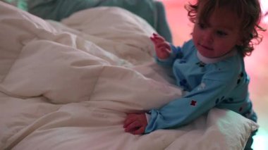 Meraklı çocuk kendini yatağa çekiyor ve yastıkların üzerinde sürünüyor, enerjik çocukluk hareketi ve yurtiçinde bağımsızlık.