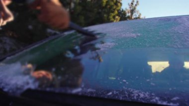 Donmuş ön camları temizleyen buz kazıyıcının yakın görüntüsü, araba Alp dağlarında kış yolculuğuna hazırlanırken cam donuyor ve kar kaplıyor.