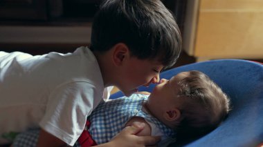 Küçük çocuk küçük kardeşlerin burnuna hafifçe dokunuyor, yumuşak bir bağ kuruyor, kardeş sevgisi, çocukluk bağı, hassas aile etkileşimi, samimi ve sevgi dolu bir sahne.