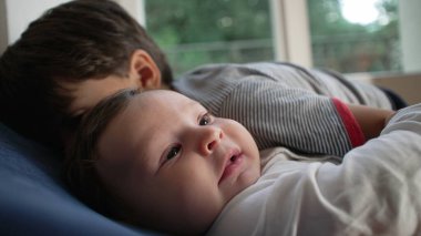 Kardeş bebek yanağına yoğun bir öpücük, sevgi dolu ama ezici kardeş etkileşimi, çocukluk yakınlığı, koruyucu kucaklama, aile sevgisi, duygusal bağ.