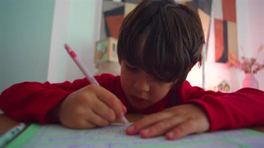 Concentrated child completing school assignment on paper, studying quietly at table with steady hand and thoughtful gaze in cozy domestic setting