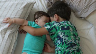 Büyük kardeş yatakta kucaklaşır, yakın kucaklaşma, sevgi dolu kardeş bağı, hassas bağ, sıcak yuva kurma, sıcak aile anı, bakım.