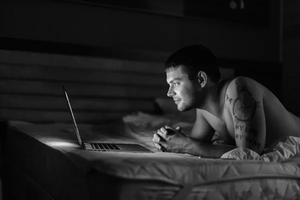dizüstü bilgisayar ile yatakta çıplak gövde ile genç adam / siyah ve beyaz fotoğraf