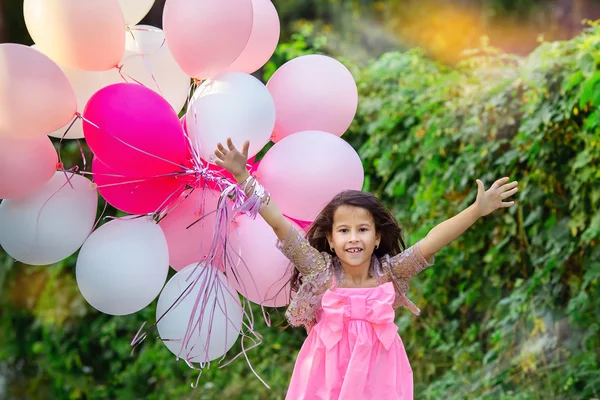 Menina encantadora em um vestido rosa inteligente vai se encontrar com um grande grupo de balões rosa . — Fotografia de Stock