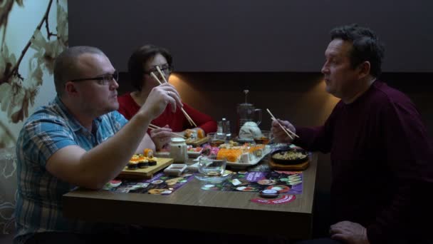 Una mujer y dos hombres comen sushi y panecillos — Vídeos de Stock