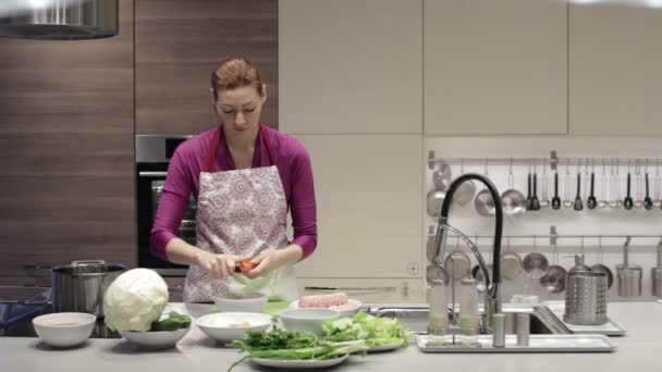 Nő konyhában egy késsel, hogy tisztítsa meg a sárgarépát — Stock videók