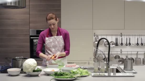 The woman in kitchen with a knife to clean carrots — Stock Video