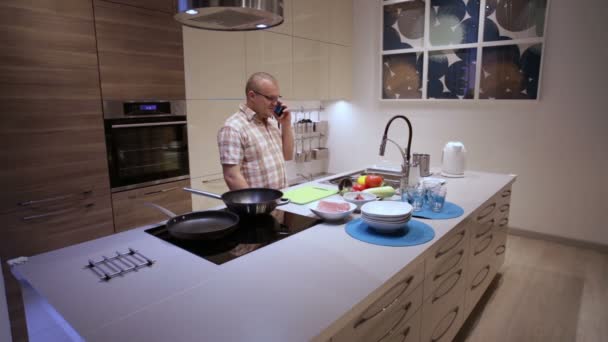 Man gaat koken in de keuken en de telefoon praten — Stockvideo