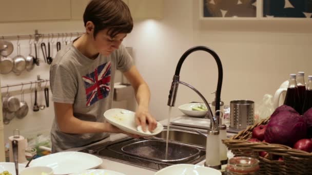 Мальчик-подросток моет тарелку в раковине — стоковое видео