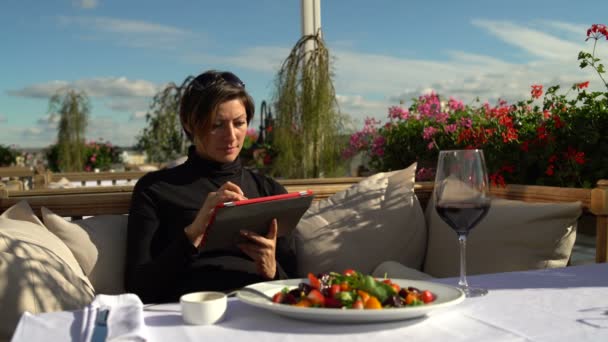 Una mujer en el restaurante terraza utiliza tableta — Vídeo de stock