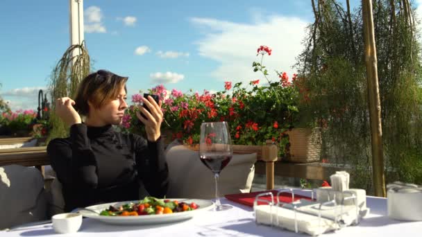 Женщина выпрямляет волосы и смотрит в зеркало на террасе ресторана — стоковое видео