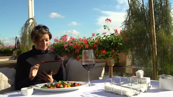Жінка насолоджується планшетом на терасі красивий ресторан — стокове відео