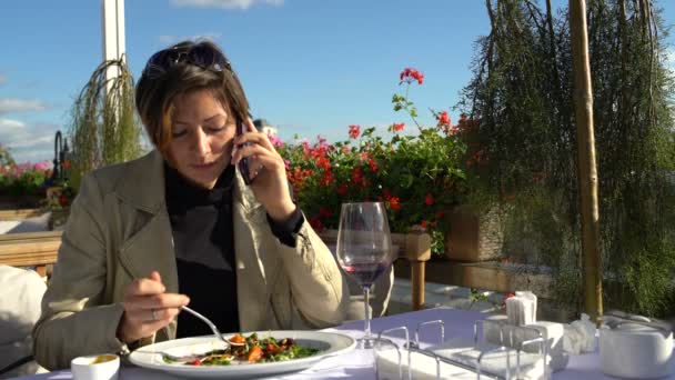 Mujer hablando por teléfono y come ensalada en un restaurante — Vídeos de Stock