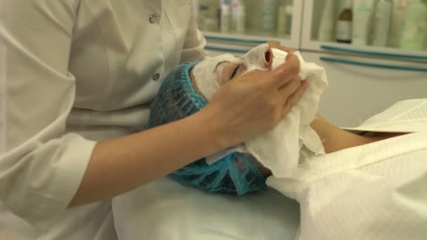 Косметолог удаляет белый крем с лица женщины — стоковое видео