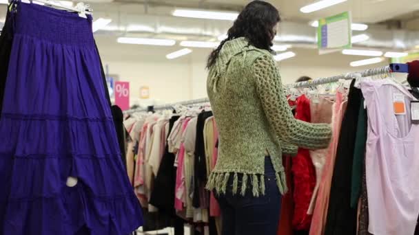 Mujer elige un vestido en la tienda — Vídeo de stock