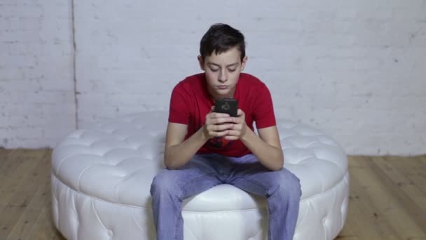 Хлопчик сидить на дивані і використовує смартфон — стокове відео