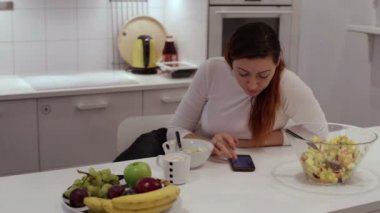 Kız masada meyve salatası yemek telefon ile oturuyor.