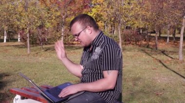 Adam laptop konuşurken parktaki bir bankta oturur