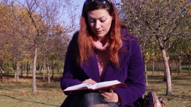 Женщина, читающая книгу на скамейке в парке — стоковое видео