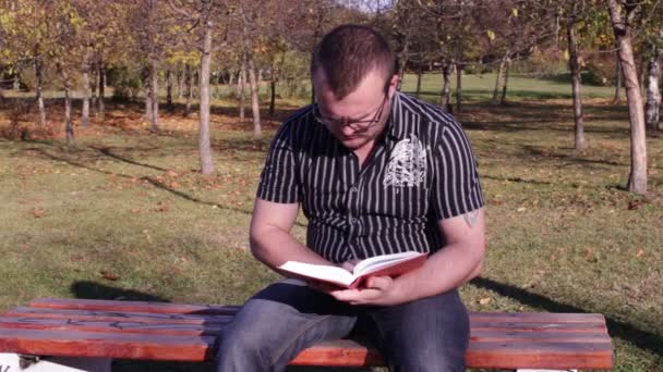 Человек, читающий книгу на скамейке в парке — стоковое видео