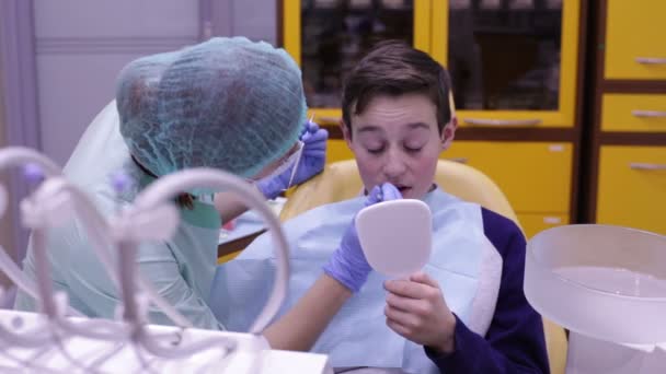 Έφηβος κοιτάζει στον καθρέφτη, όπως ο οδοντίατρος εξετάζει τα δόντια — Αρχείο Βίντεο