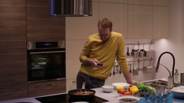 Man met behulp van smartphone en koken in de keuken — Stockvideo