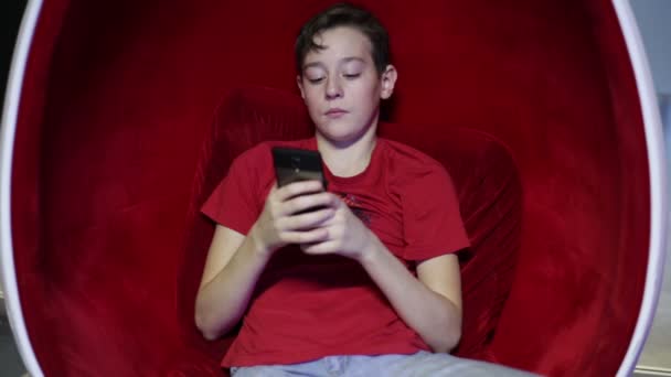 Adolescente sentada en una silla en forma de huevo con teléfono — Vídeos de Stock