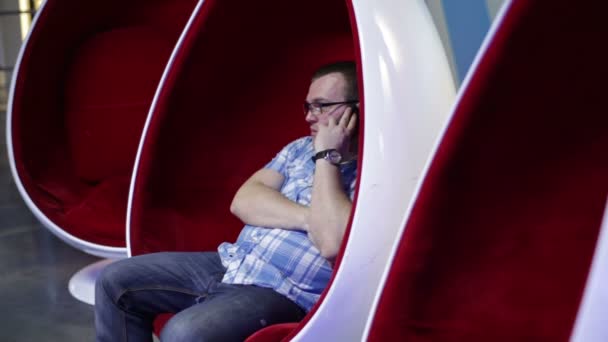 Мужчина разговаривает по телефону в яйцевидном кресле — стоковое видео