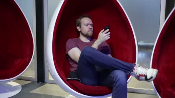 Man schrijft sms in een ei-vormige stoel — Stockvideo