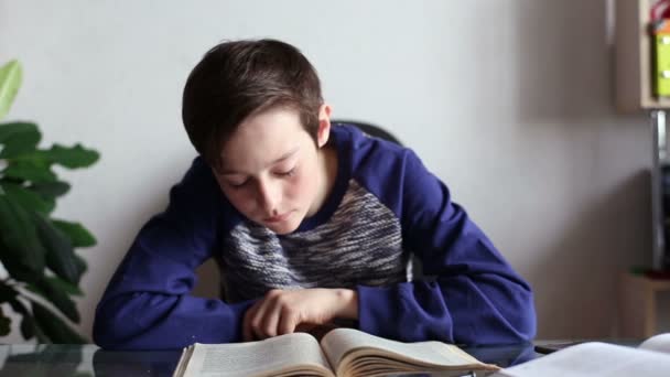 Adolescente chico leyendo un libro en la mesa en casa — Vídeo de stock