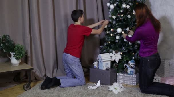 女性と 10 代の少年がクリスマス ツリーをドレスアップします。 — ストック動画