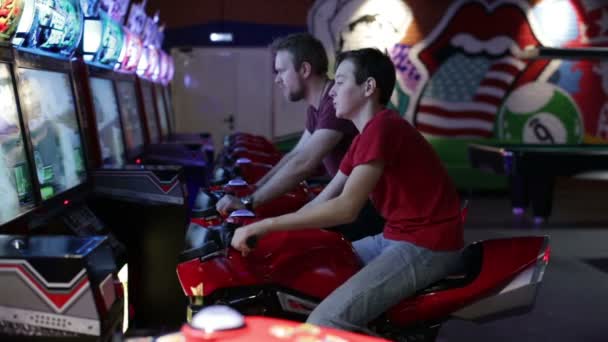 Two men playing arcade racing game on moto — Stock Video