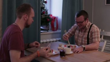 Suşi çubukla yemek masasında oturan adam