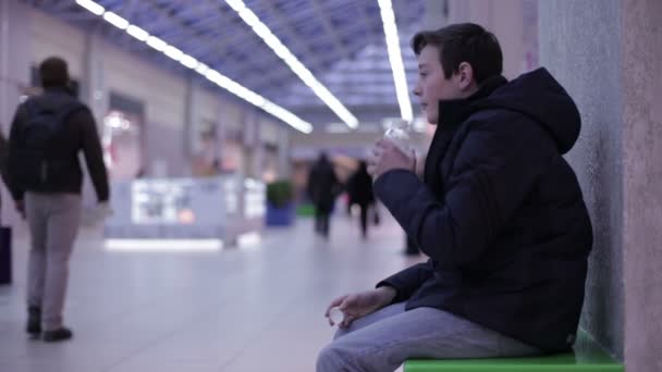 Подросток сидит на скамейке и пьет лимонад — стоковое видео